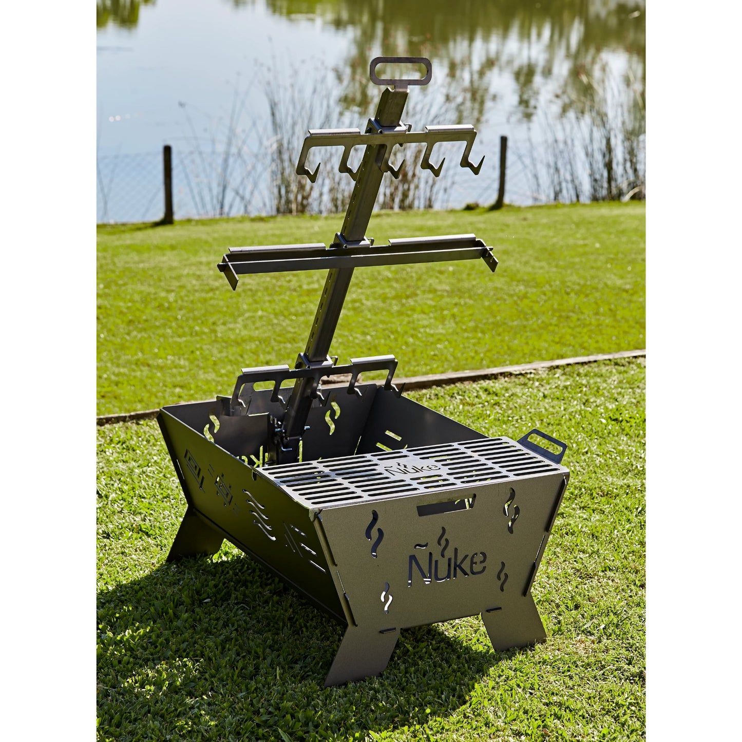 Portable grill with 'Nuke' branding on a grassy area by a body of water.