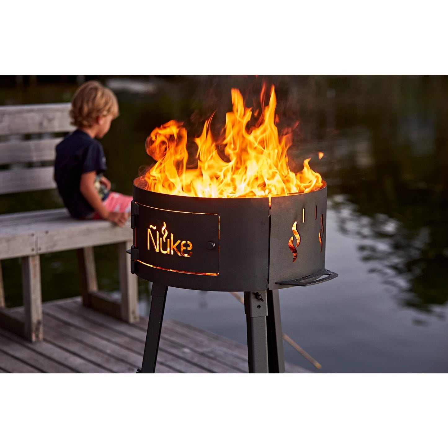 Fire pit with flames on a wooden deck, person sitting on a bench in the background