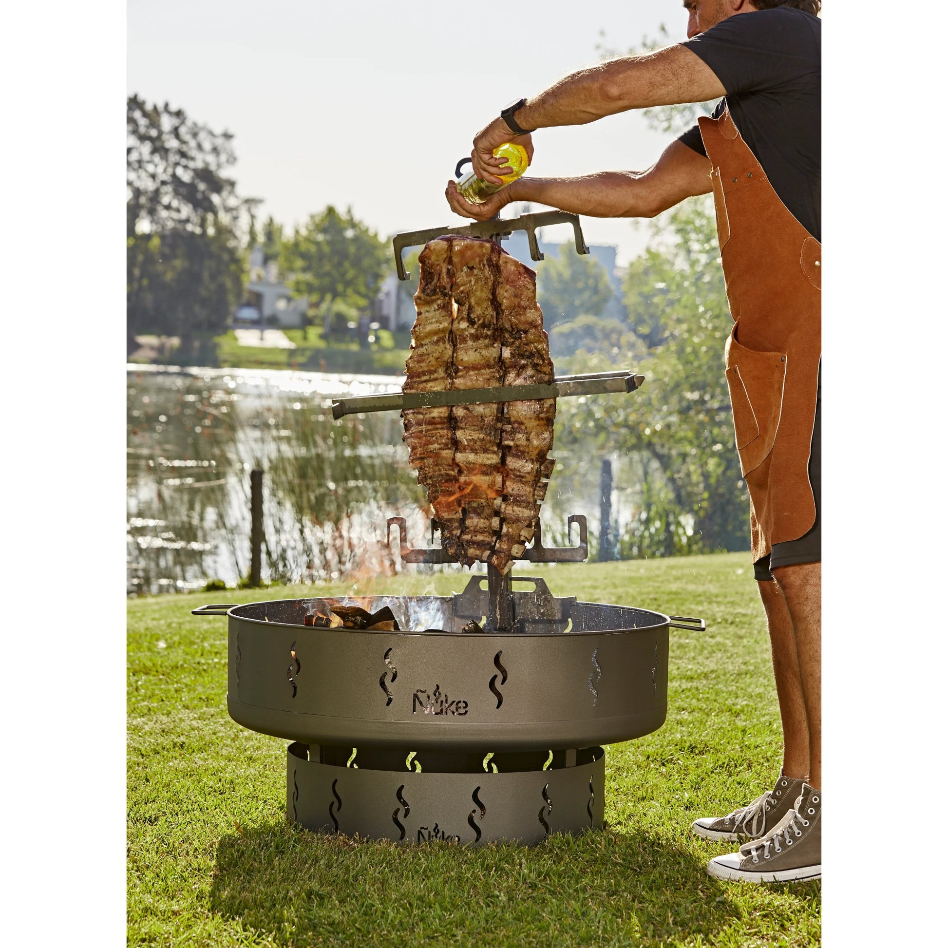 Person grilling meat over a fire pit by a lake