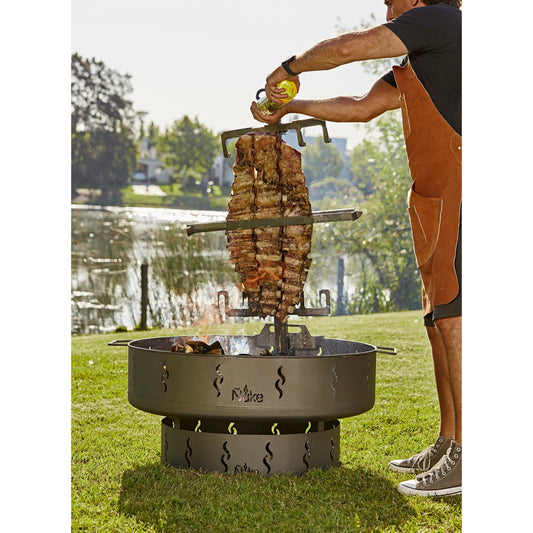Person grilling meat over a fire pit by a lake